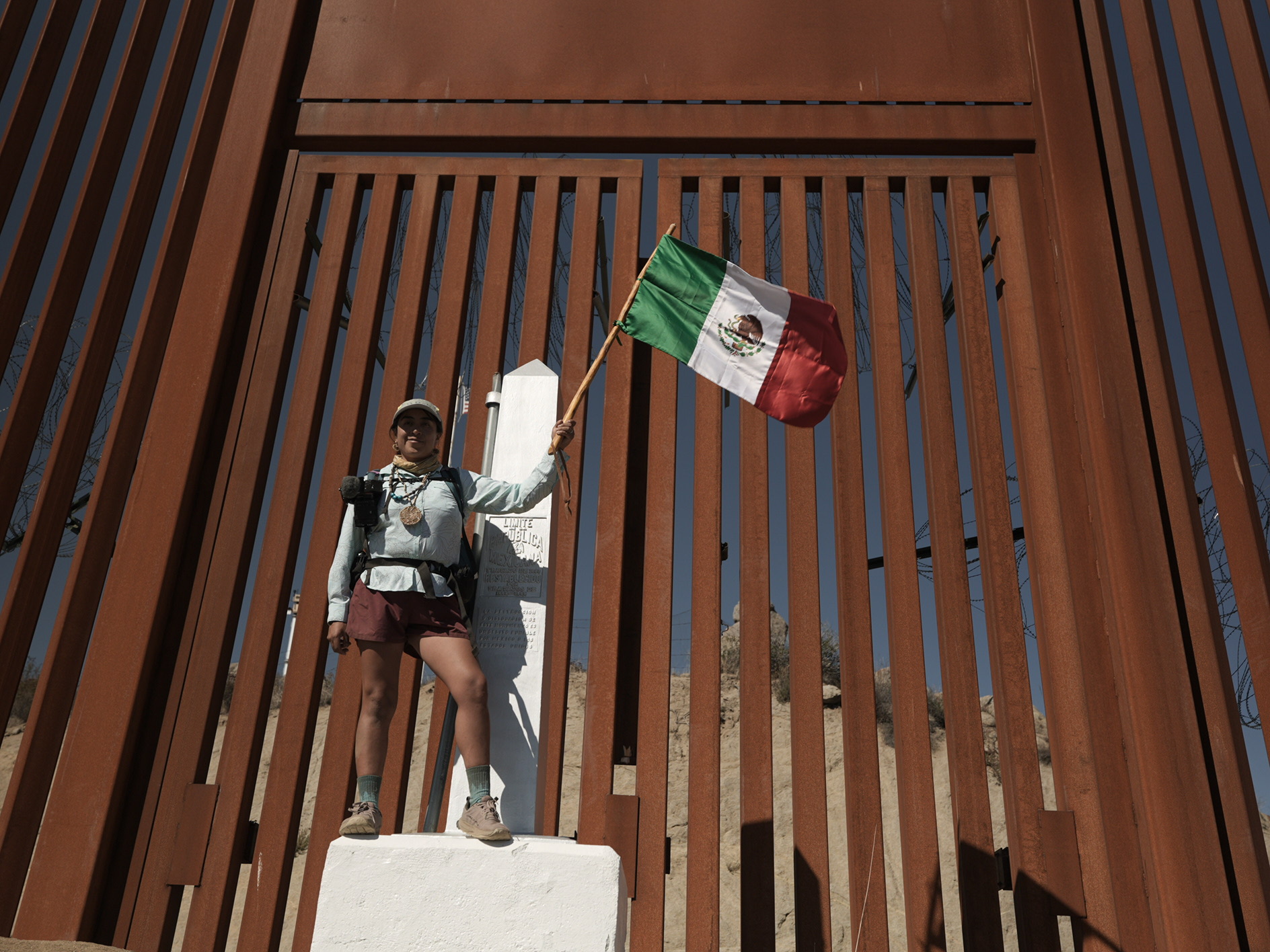 Woman standing triumphantly at trail terminus on Mexico-US border with Mexican flag