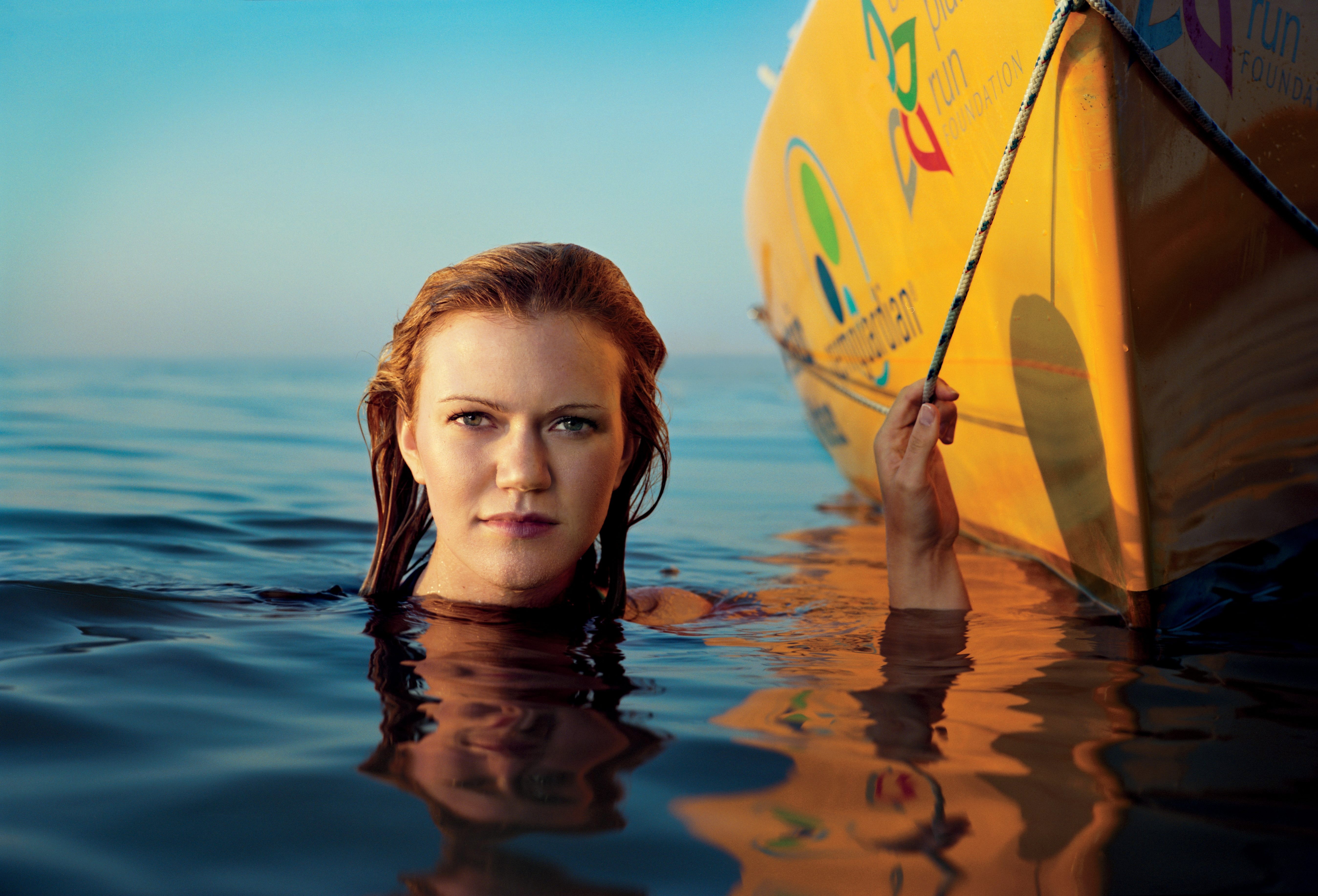Woman in ocean next to yellow kayak with head above water looking into camera